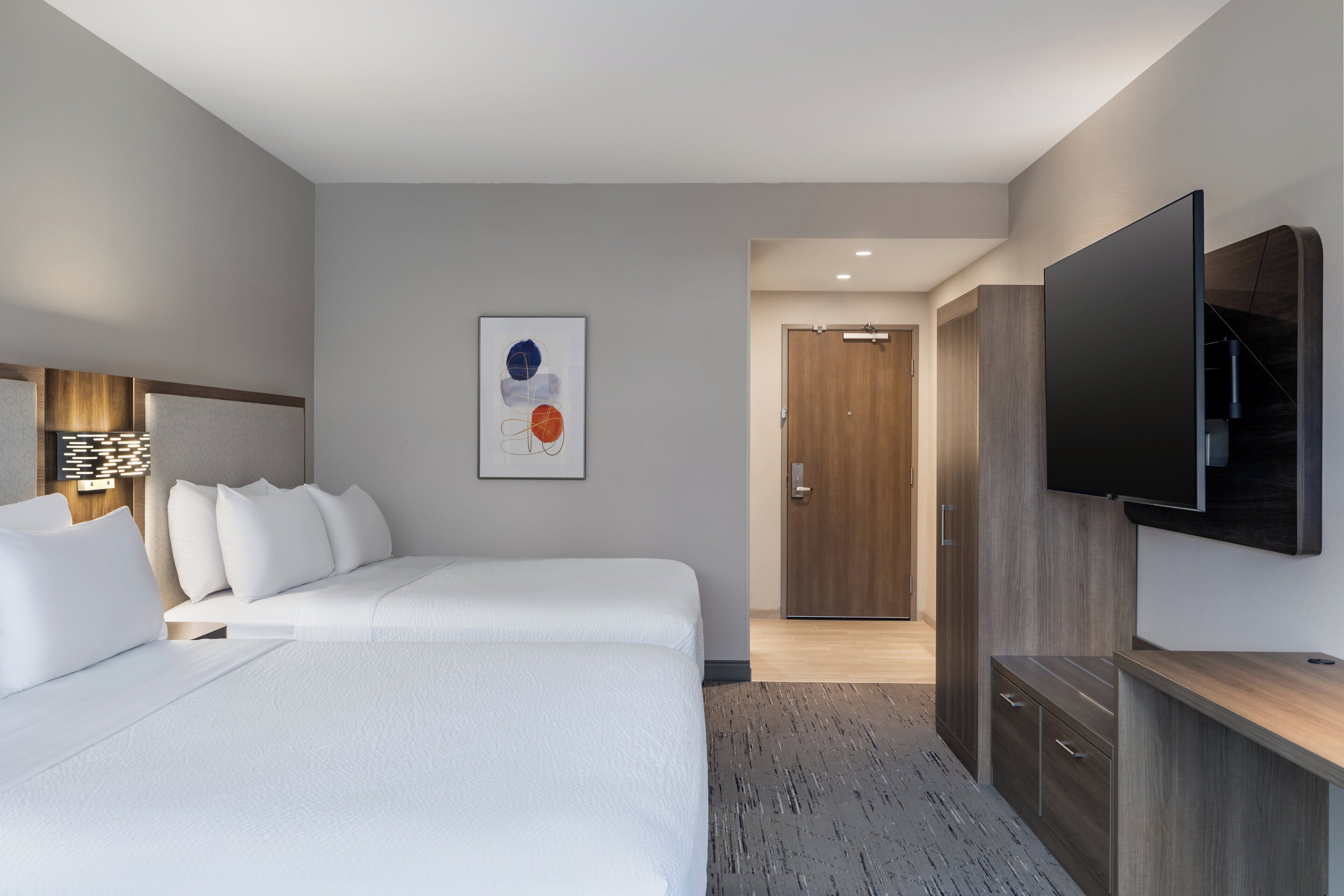 A modern hotel room with a large bed, a flat-screen TV mounted on the wall, and a wooden wardrobe.