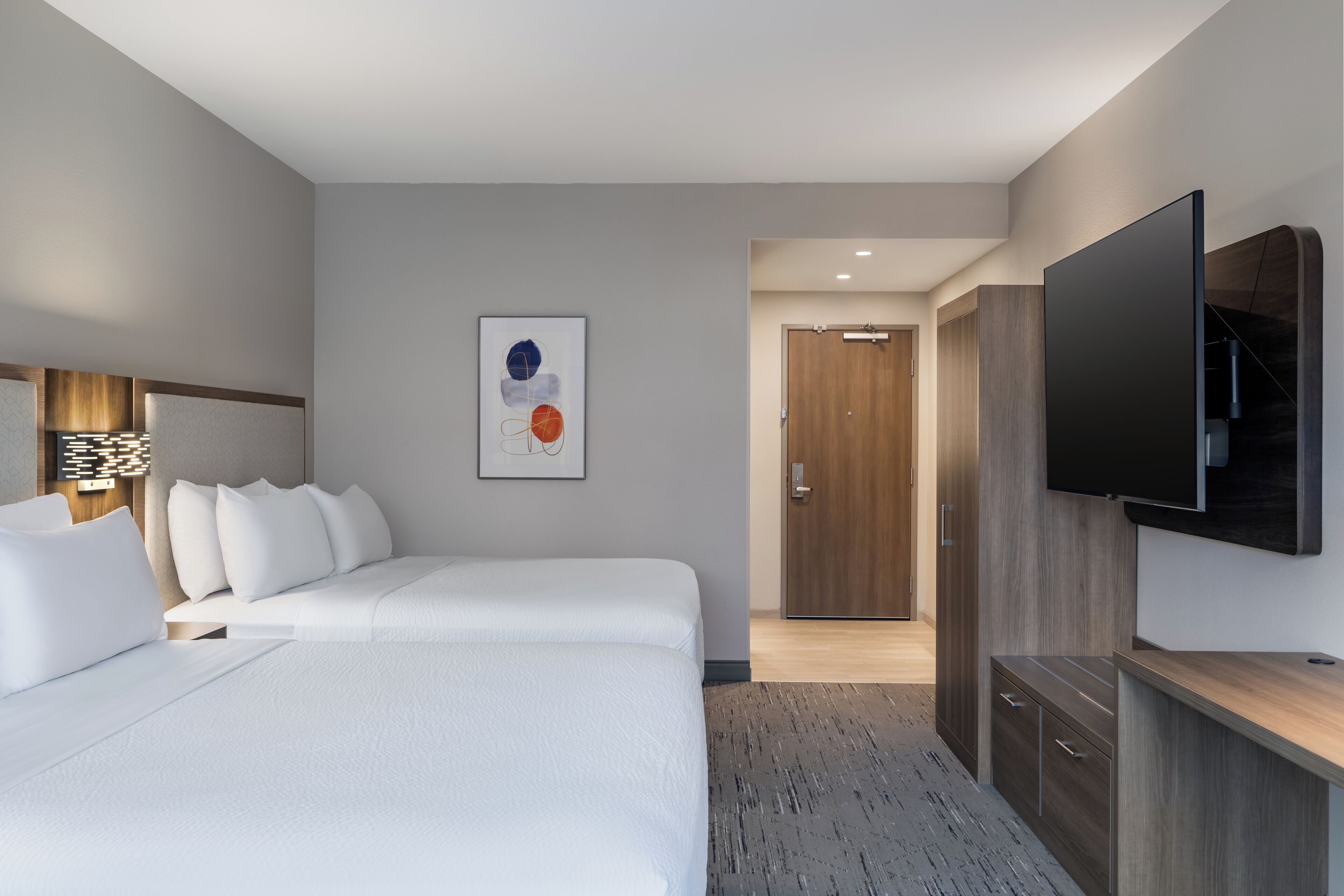 Quarto de hotel moderno com uma cama grande, uma televisão de tela plana na parede e um guarda-roupa de madeira.