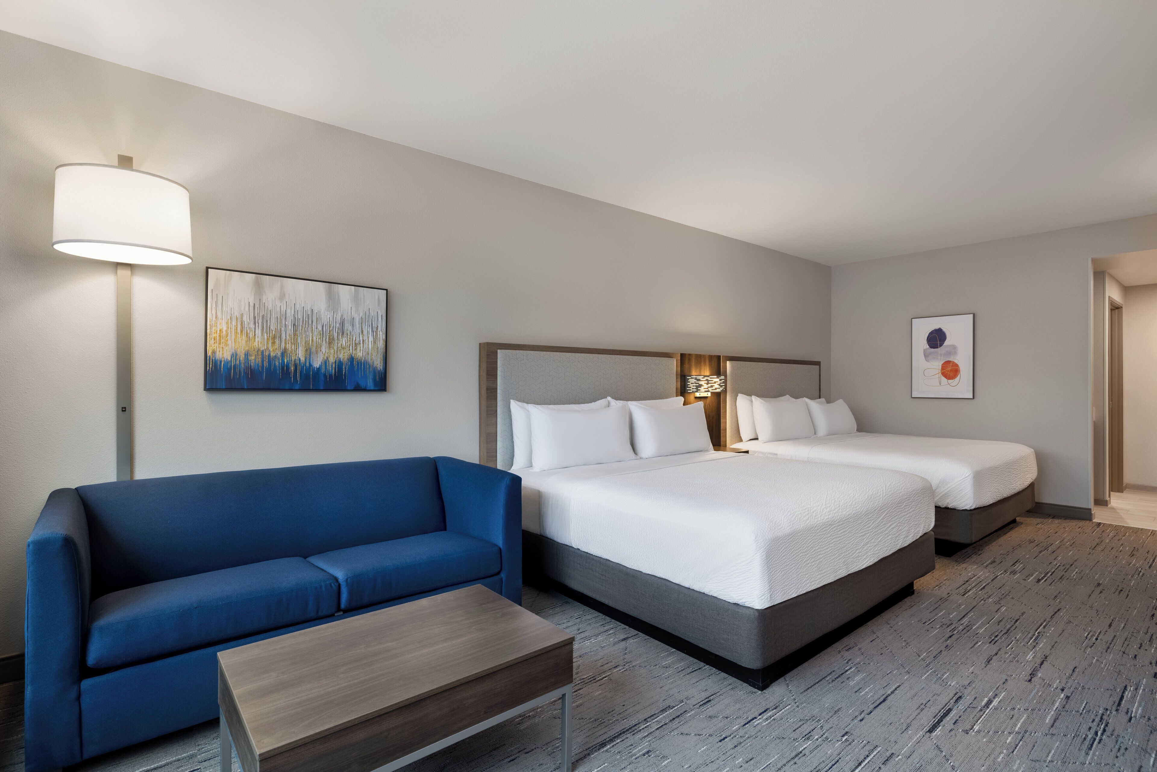 Ein Hotelzimmer mit einem blauen Sofa, zwei Einzelbetten, einem Holztisch und Kunstwerken an den Wänden.