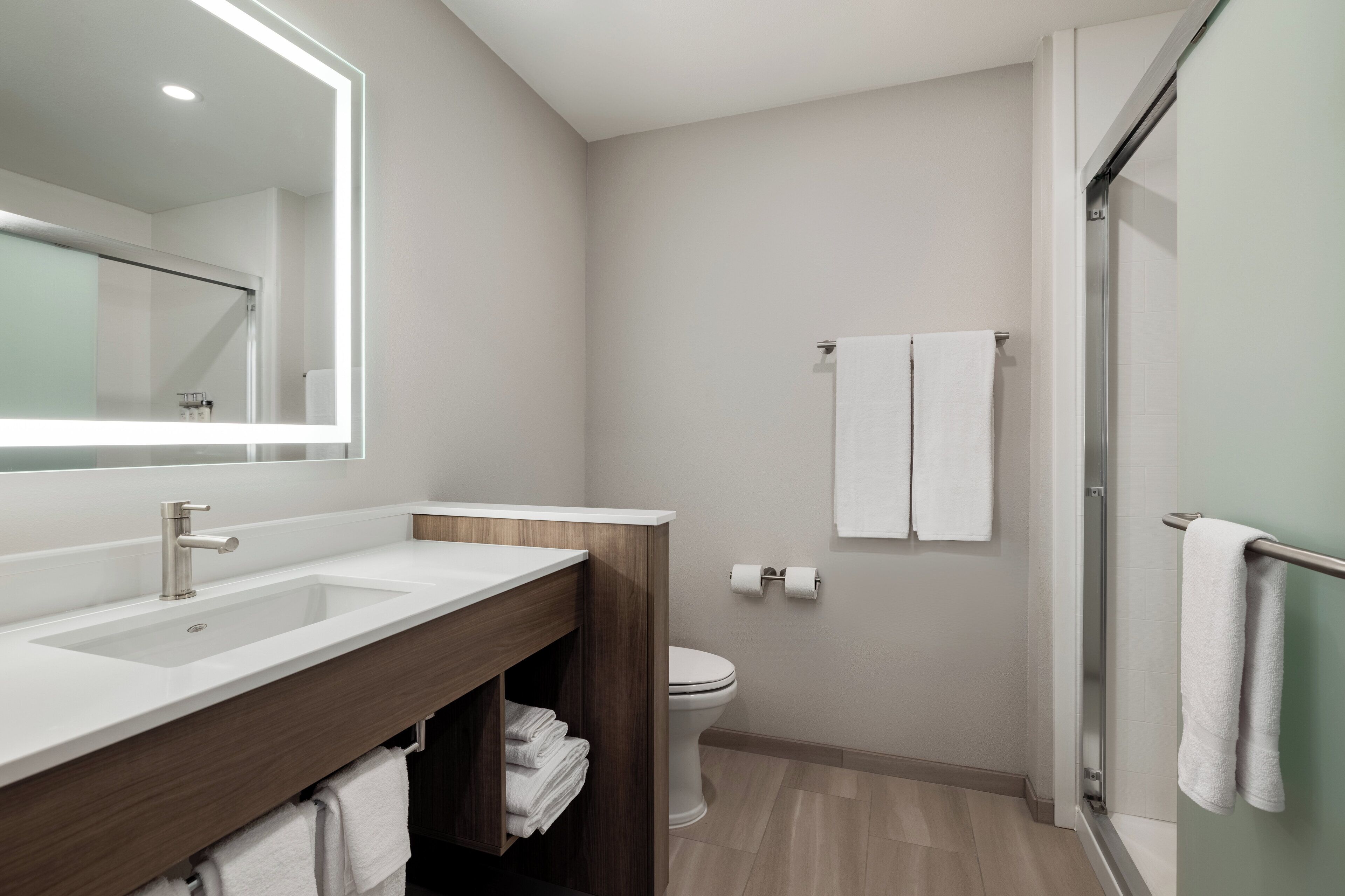 A modern bathroom with a large mirror, two sinks, a toilet, and a shower area.