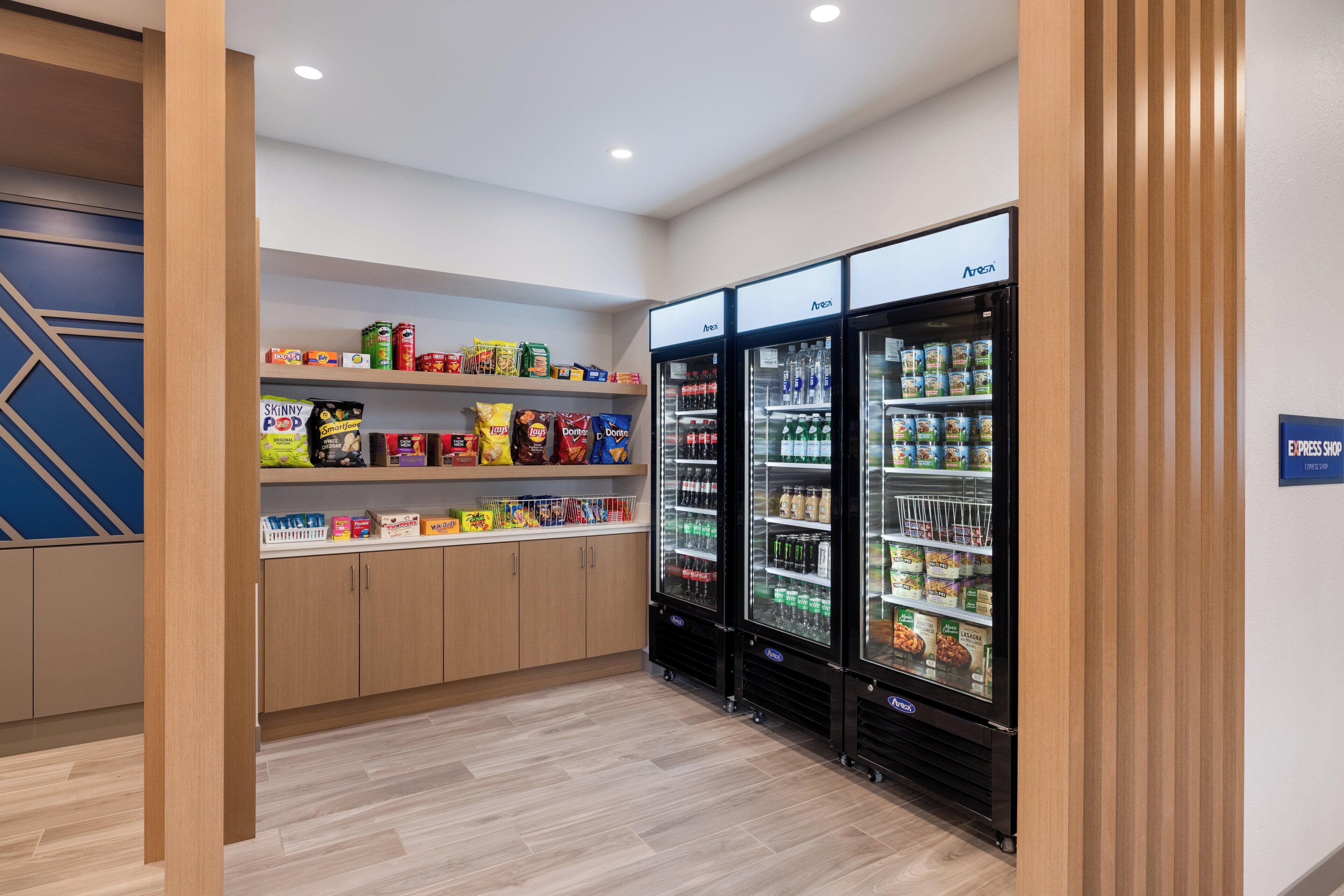 A clean, modern room with wooden cabinets and a snack shelf stocked with various snacks.