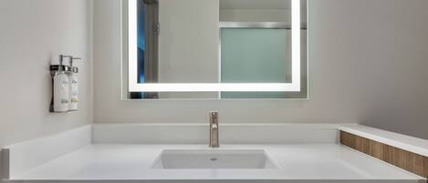 A modern bathroom with a white sink, a large mirror, and a wooden vanity.