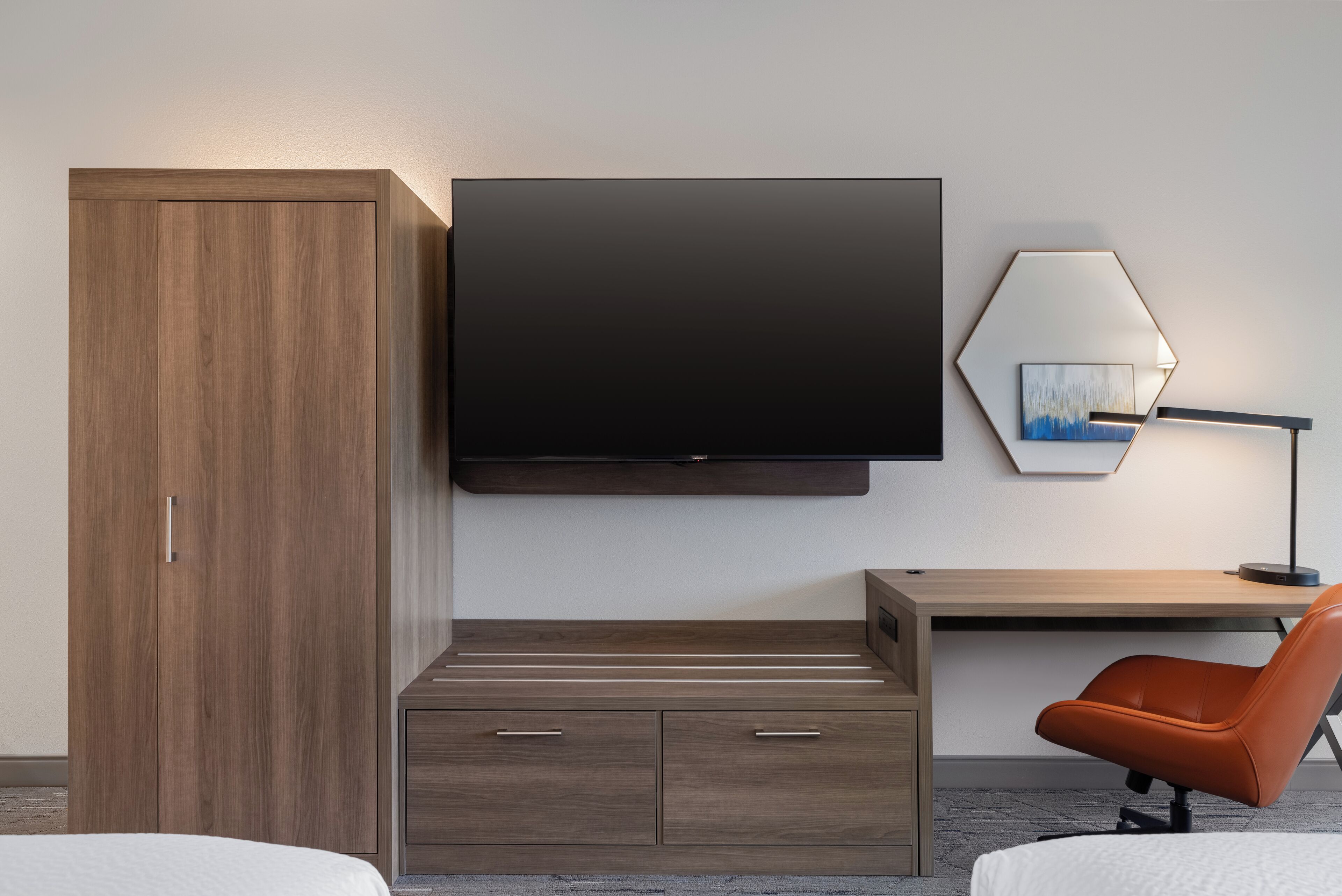 Een moderne hotelkamer met een houten garderobe, een flatscreen televisie, een bureau met stoel en een lamp.