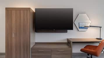 Een moderne hotelkamer met een houten garderobe, een flatscreen televisie, een bureau met stoel en een lamp.