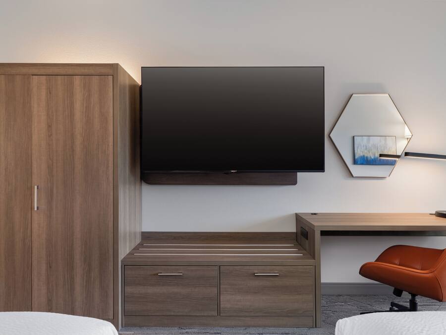 Een moderne hotelkamer met een houten garderobe, een flatscreen televisie, een bureau met stoel en een lamp.