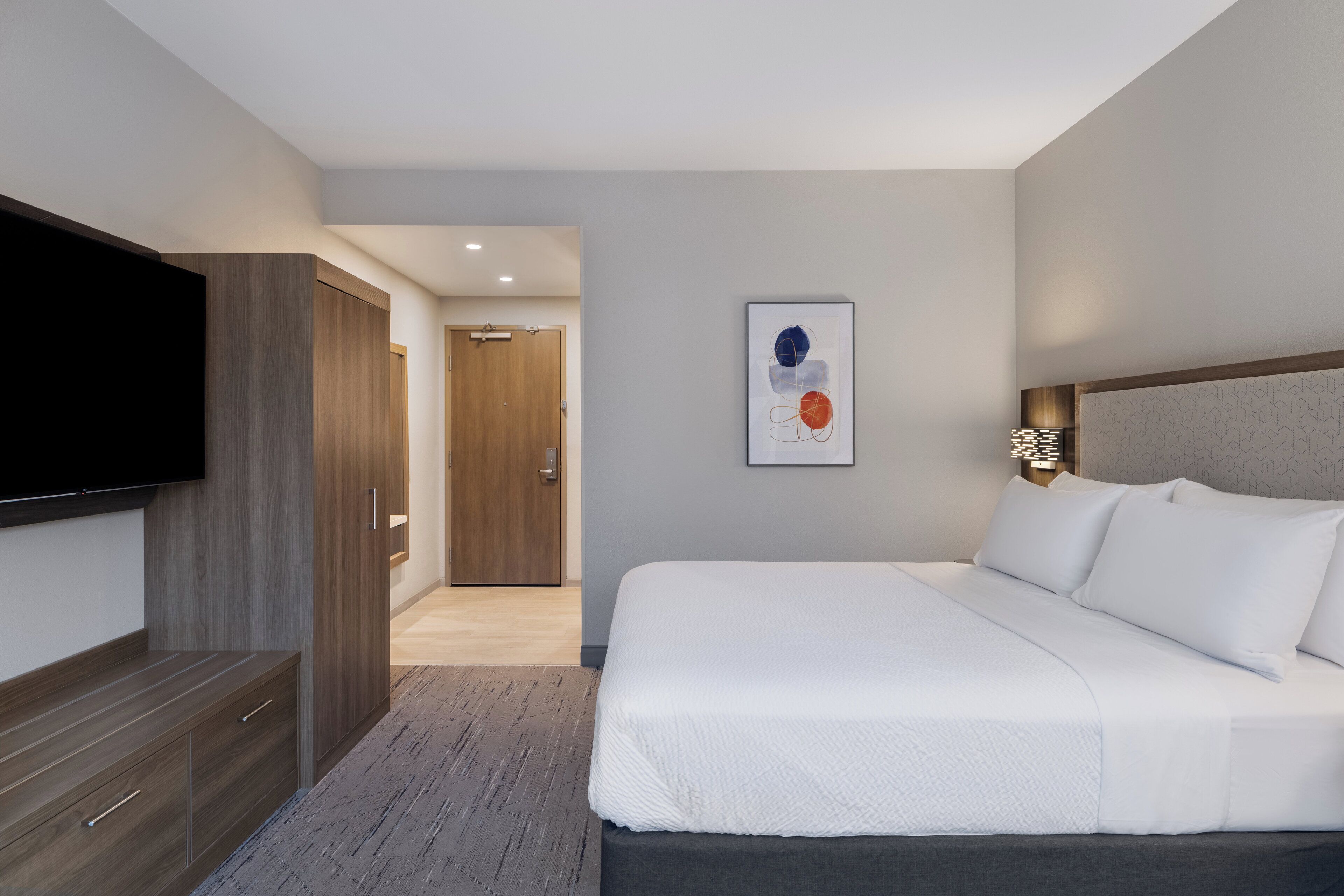 A modern hotel room with a large bed, a flat-screen TV, a wardrobe, and a door leading to another room.