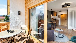 A wooden deck with a table and chairs, a glass door leading to a kitchen, and a cozy seating area with a rug. - Cozy top floor studio with pool & sauna (Reit im Winkl)
