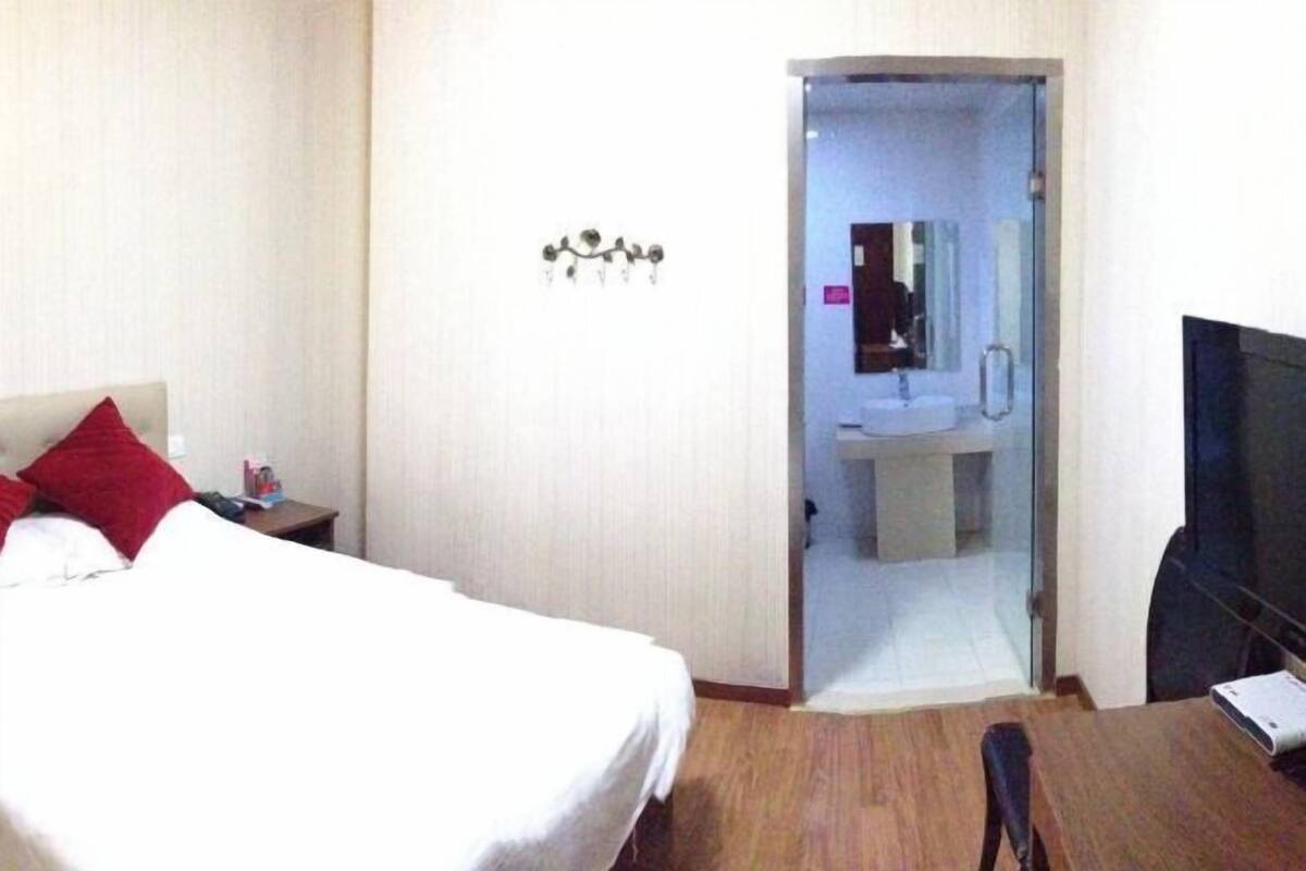 A hotel room with a bed, a desk, a TV, and a bathroom visible through an open door.