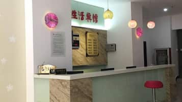 Balcão de recepção com painel de madeira, uma luminária de neon e um banquinho vermelho.
