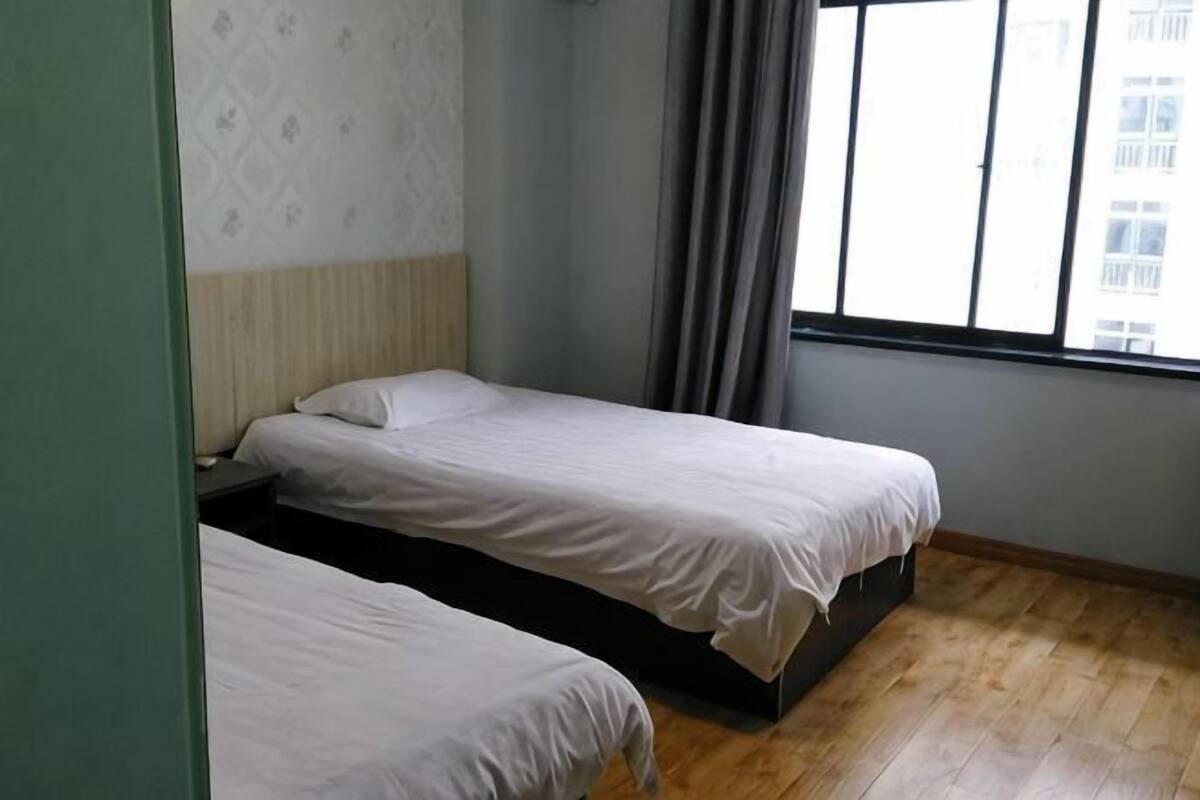 A room with two beds, a window with curtains, and a patterned wall.