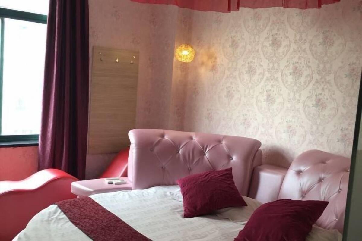 A bedroom with a tufted headboard, a bedside table, and a window with curtains.