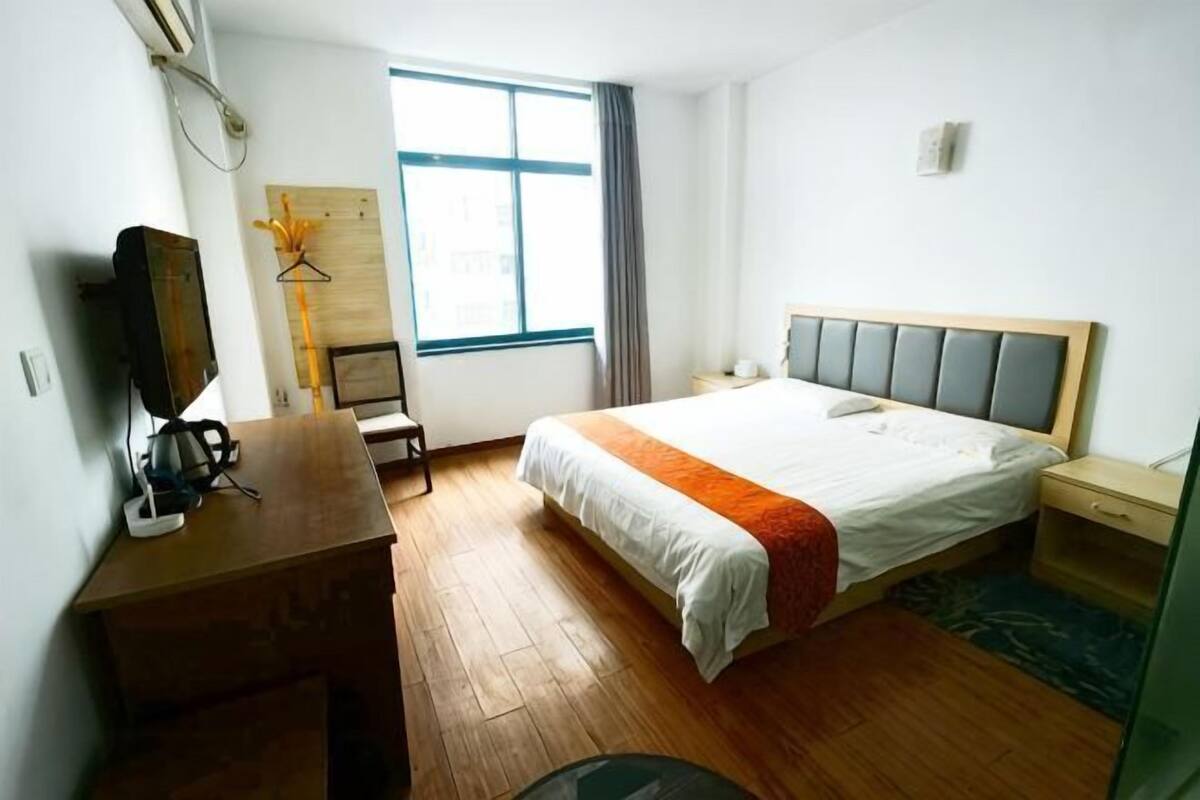 A hotel room with a bed, a desk, a chair, a television, a window, and a wardrobe.