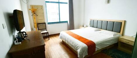 A hotel room with a bed, a desk, a chair, a television, a window, and a wardrobe.