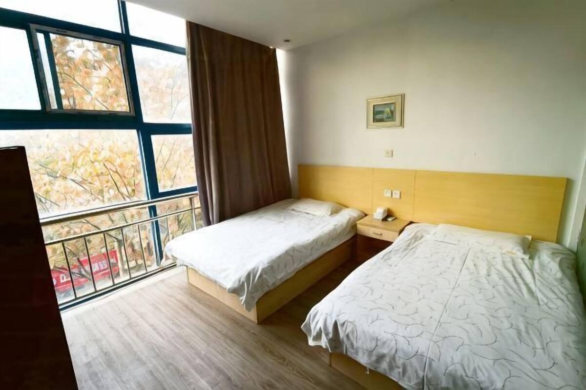 A room with two beds, a window with a view, a wooden headboard, and a small bedside table.