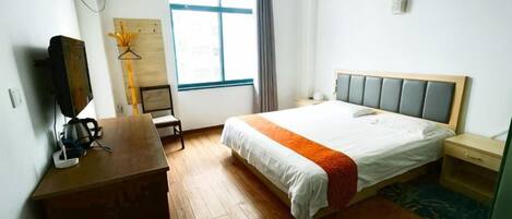 A hotel room with a bed, a desk, a chair, a TV, and a window.