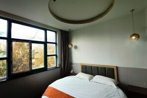 A bedroom with a large window, a bed with white and orange bedding, a round ceiling light, and a nightstand with a lamp. - Meilu Living Hotel (Shanghai)