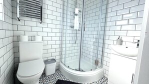 Ein modernes Badezimmer mit weißen, rechteckigen Fliesen, einer Duschkabine aus Glas, einer weißen Toilette und einem Waschbecken mit Spiegel.