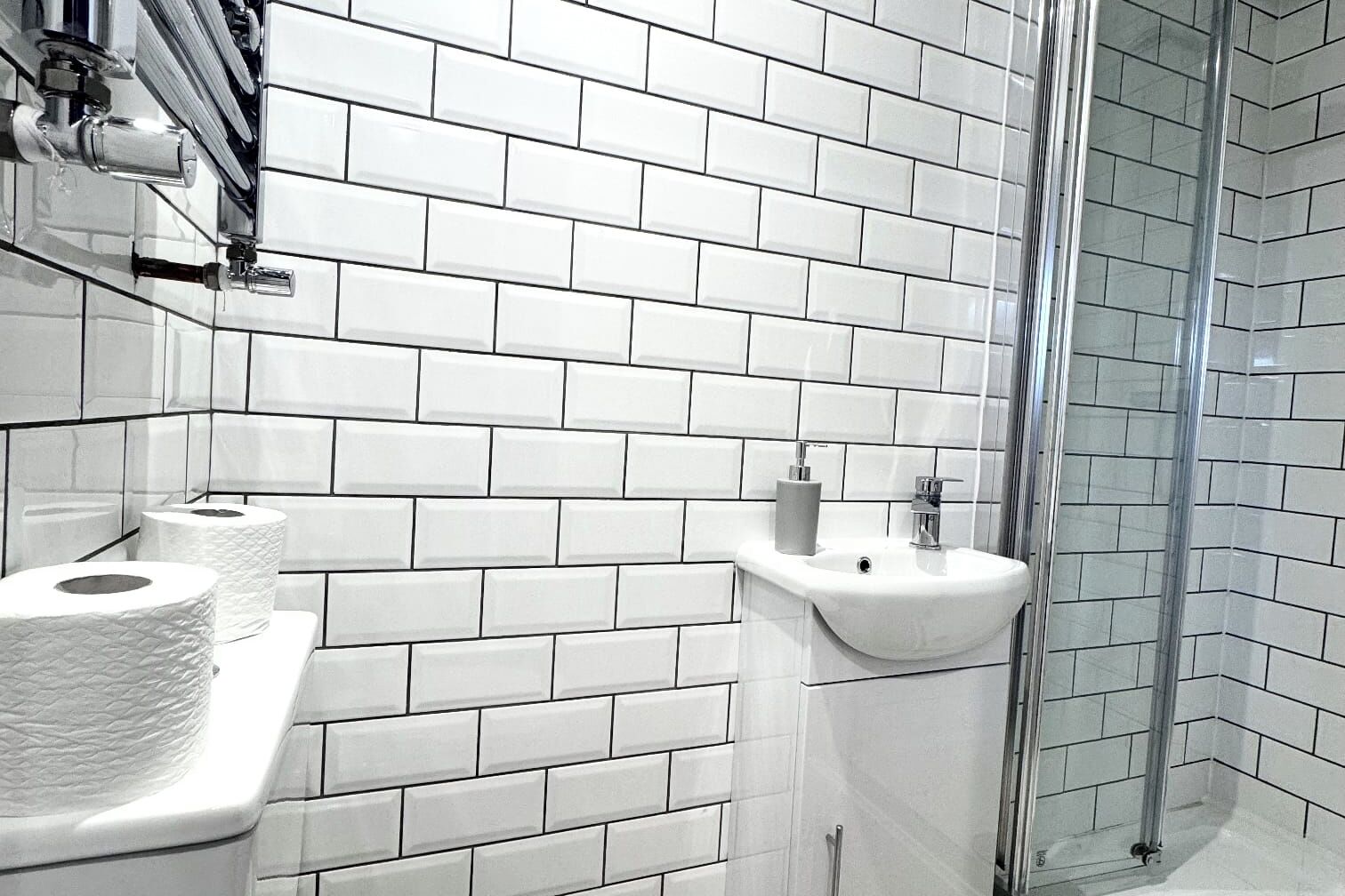 A bathroom with white subway tiles, a sink, a toilet, and a glass shower enclosure.