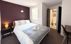 A bedroom with a bed, bedside table, lamp, and a wall-mounted sign.