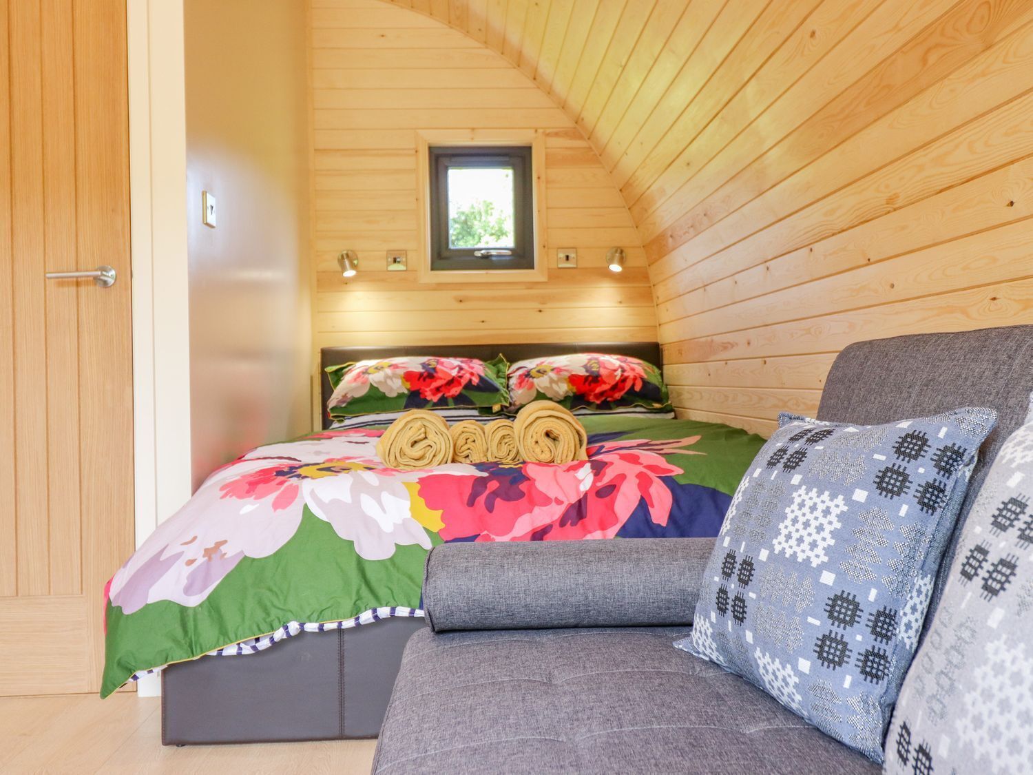 A cozy wooden cabin bedroom with a bed, a sofa, and a small window.