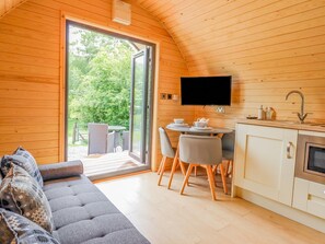 Interior acogedor de una cabaña con sofá, mesa de comedor, sillas, televisor y zona de cocina.