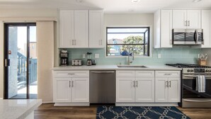 Una cocina moderna con armarios blancos, un refrigerador de acero inoxidable, horno empotrado y ventana que proporciona luz natural.