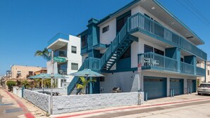 Un edificio de varios pisos con una combinación de colores azul y blanco, un garaje visible y sombrillas en el exterior.