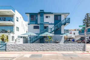 Un b âtiment à deux étages, à la façade bleue et blanche, avec un escalier apparent et des parasols à l’extérieur.