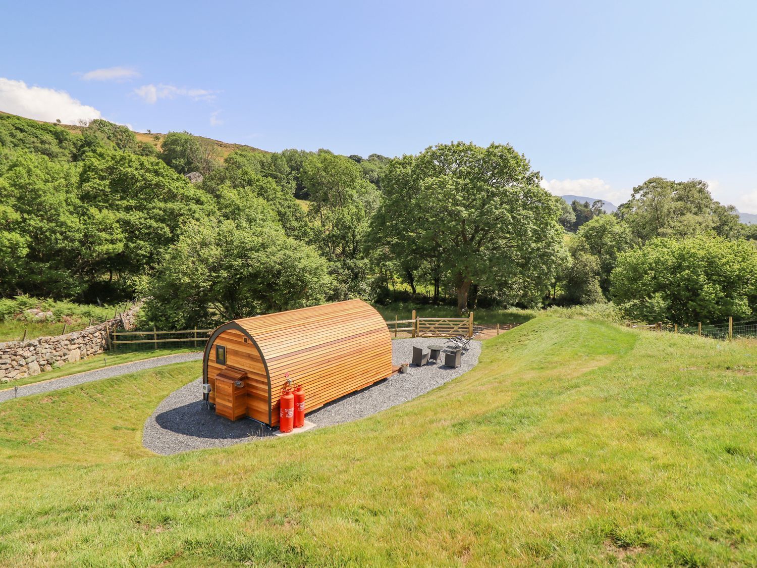 Une cabane en bois avec une allée en gravier et un espace clôturé aménagé avec des sièges d’extérieur.