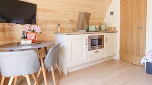 A compact kitchen with a microwave, oven, and sink. There is a dining table with chairs and a TV mounted on the wall. - Eirlys (Dolgellau)