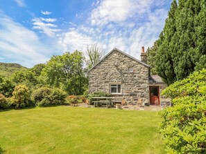 A stone house with a grassy yard, a wooden deck, and a red door. - Dwynant (Dolgellau)