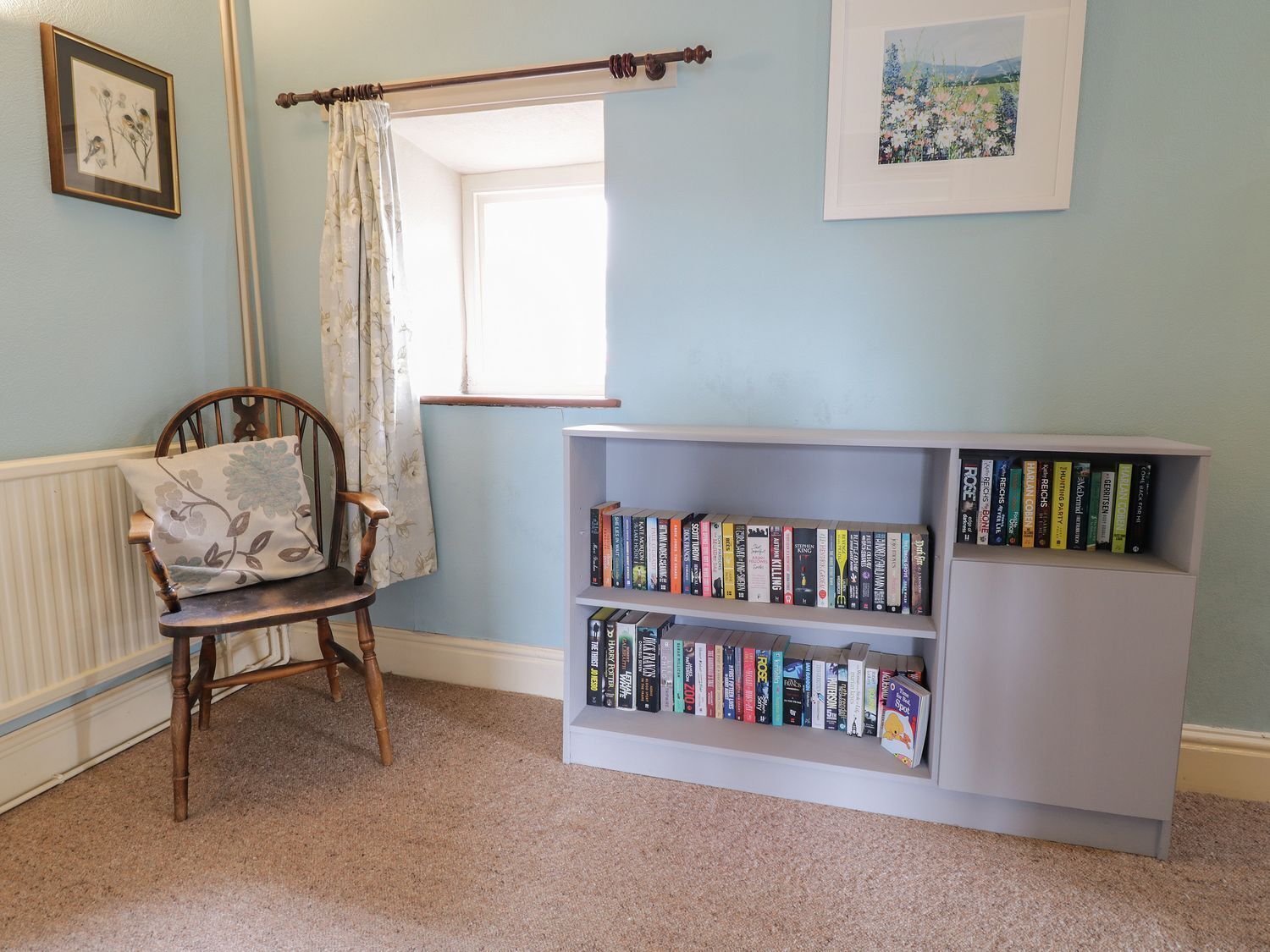 A room with a wooden chair, a bookshelf, and a window with a curtain.