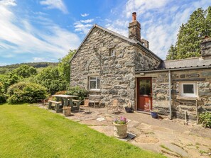 A stone house with a small patio, a wooden table, and chairs. - Dwynant (Dolgellau)