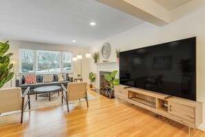 Een moderne woonkamer met een grote flatscreen televisie, houten vloeren, een open haard en een bank met opvallende kussens.