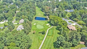 Luftaufnahme eines Golfplatzes mit Teich, umgeben von Wohngebäuden.