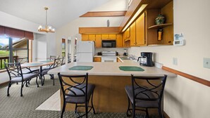 Una cocina moderna con armarios de madera, una isla central con taburetes de bar, un área de comedor con mesa y sillas, y vistas al exterior.