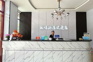 Un mostrador de recepción de hotel con encimera de mármol, una computadora y un letrero con caracteres chinos.