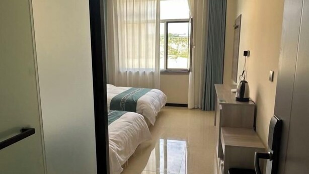 Une chambre d’hôtel avec deux lits, une fenêtre avec des rideaux, un petit bureau avec une chaise et une poubelle.
