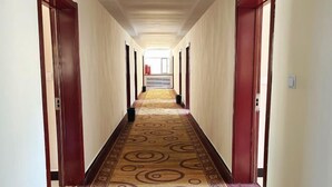 Un couloir d’hôtel avec un tapis à motifs, des portes en bois et un mur de couleur claire.
