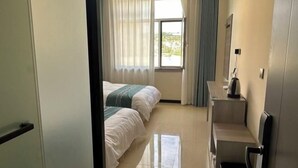 Une chambre d’hôtel avec deux lits, une fenêtre avec des rideaux, un petit bureau et une poubelle.