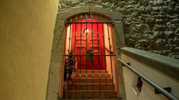 Eine Treppe führt zu einer roten Tür mit schmiedeeisernem Gitter.