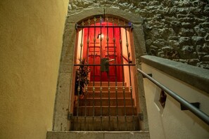 Un escalier menant à une porte rouge, surmontée d’un portail en fer forgé.