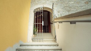 Eine Treppe führt zu einer Tür mit einem Metallgitter, einem Kachelboden und einer Steinwand.