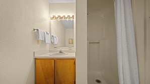 Une salle de bain avec un meuble-lavabo en bois, un évier, un miroir avec éclairage intégré et un espace douche.