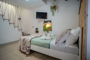 Une chambre à coucher moderne avec un lit, un téléviseur fixé au mur, une petite étagère avec une lampe et une plante suspendue.