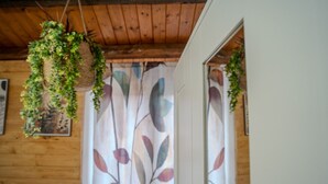 A wooden interior with hanging plants, a patterned curtain, and a white door.