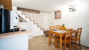 A compact kitchen with a coffee maker, a dining table with chairs, and a fruit basket.