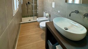 A modern bathroom with a large sink, two toilets, a glass-enclosed shower, and a wooden floor. - The Romantic Apartment for two (Naples)