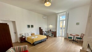 A hotel room with a bed, a desk, a chair, a small table, and a sofa. - The Romantic Apartment for two (Naples)