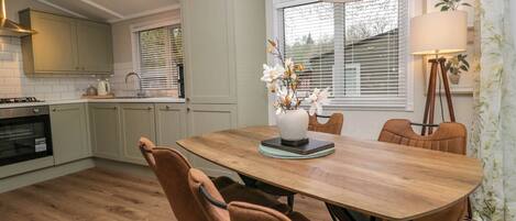A modern kitchen with light green cabinets, a wooden dining table, and brown chairs.